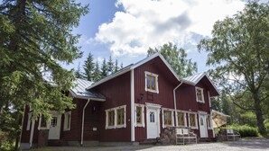 A red wooden building with a white door and windows, surrounded by trees. - Taulun Kartano (Toivakka)