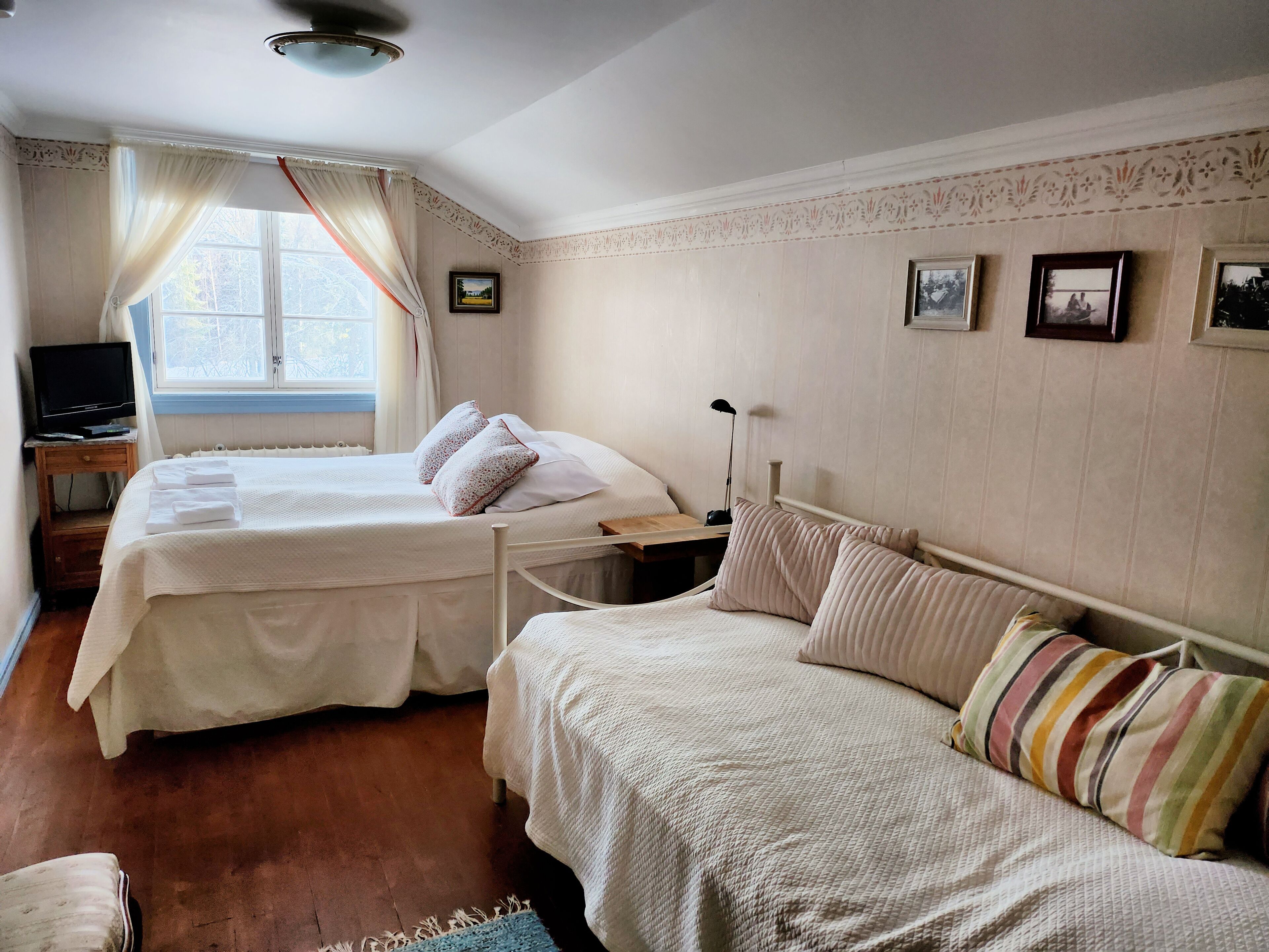 A bedroom with two beds, a TV on a stand, and a window with curtains.