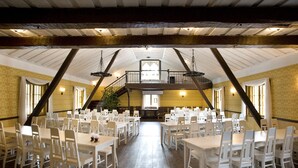 A spacious hall with multiple white tables and chairs, a balcony, and a staircase leading to an upper level. - Taulun Kartano (Toivakka)