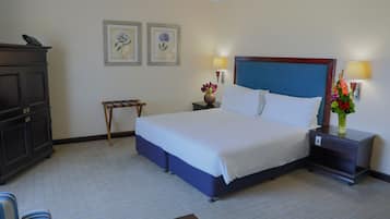 Ein Hotelzimmer mit einem großen Bett, einem Nachttisch mit Lampe, einer Kommode und zwei gerahmten Blumenbildern an der Wand.