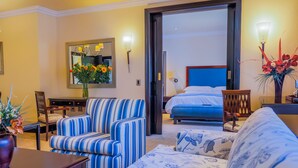 A hotel room with a bed, a striped sofa, a dining table with chairs, a chandelier, and a large mirror. - The Carousel Hotel (Hammanskraal)