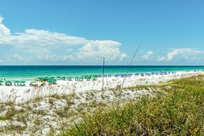 A beach with white sand, green umbrellas, and a clear blue sky.