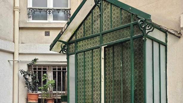 A green glass greenhouse with a door, steps leading up to it, and potted plants on a balcony. - Invalides•Tour Eiffel | Charming flat Paris Centre (Paris)