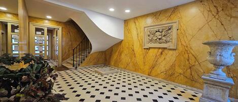 A lobby with a checkered floor, a staircase, and a decorative wall.
