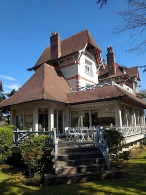 A two-story house with a prominent gabled roof, a covered porch with white railings, and a staircase leading to the entrance.