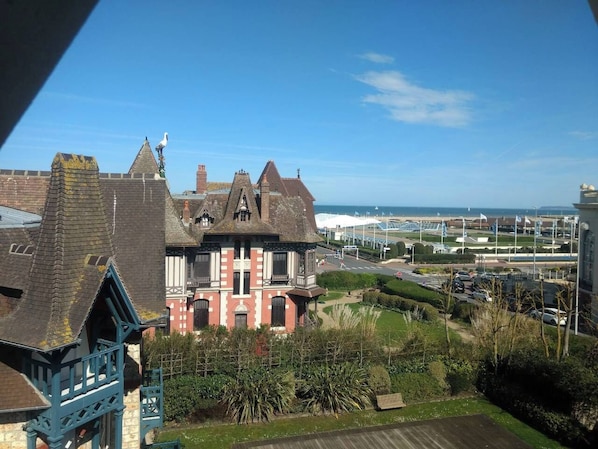 A large, historic building with multiple towers and a prominent balcony, surrounded by well-maintained gardens and a view of the sea.