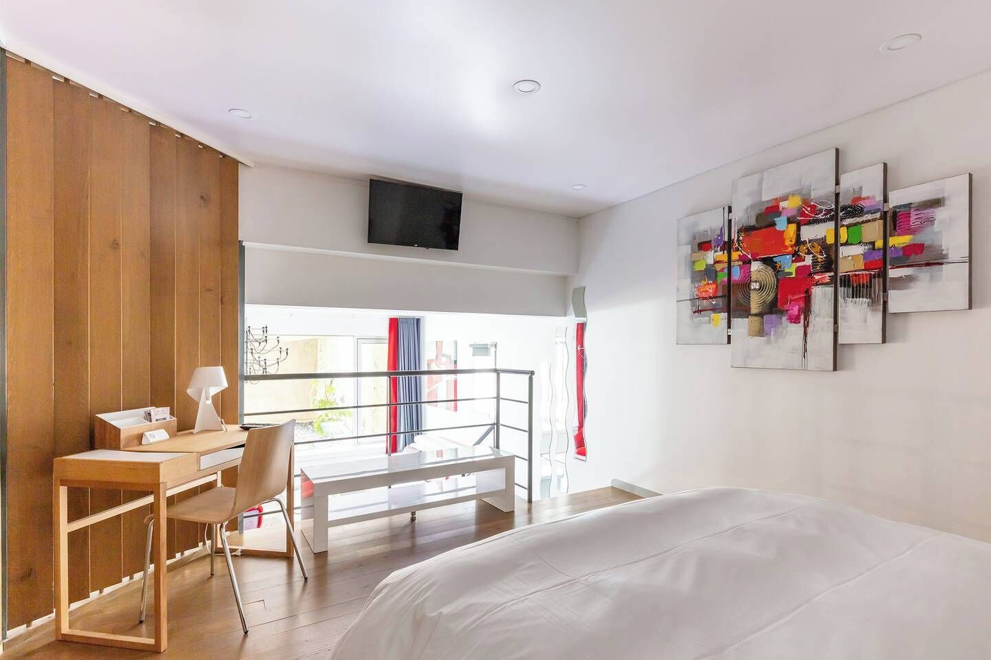 Een moderne slaapkamer met een bed, een bureau en een stoel. Er is een balkon met uitzicht op de omgeving.