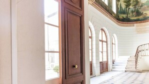 A grand entrance with a wooden door, white columns, and a staircase leading to an upper level. - Chic Designer Loft in Historic Mansion • Marais (Paris)