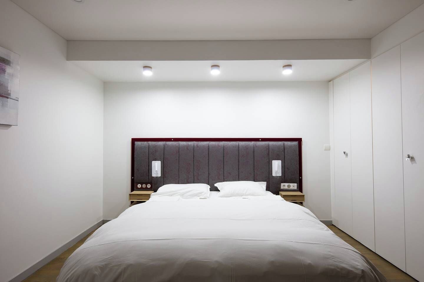 Een hotelkamer met een groot bed, een houten hoofdbord, nachtkastjes en een kledingkast.