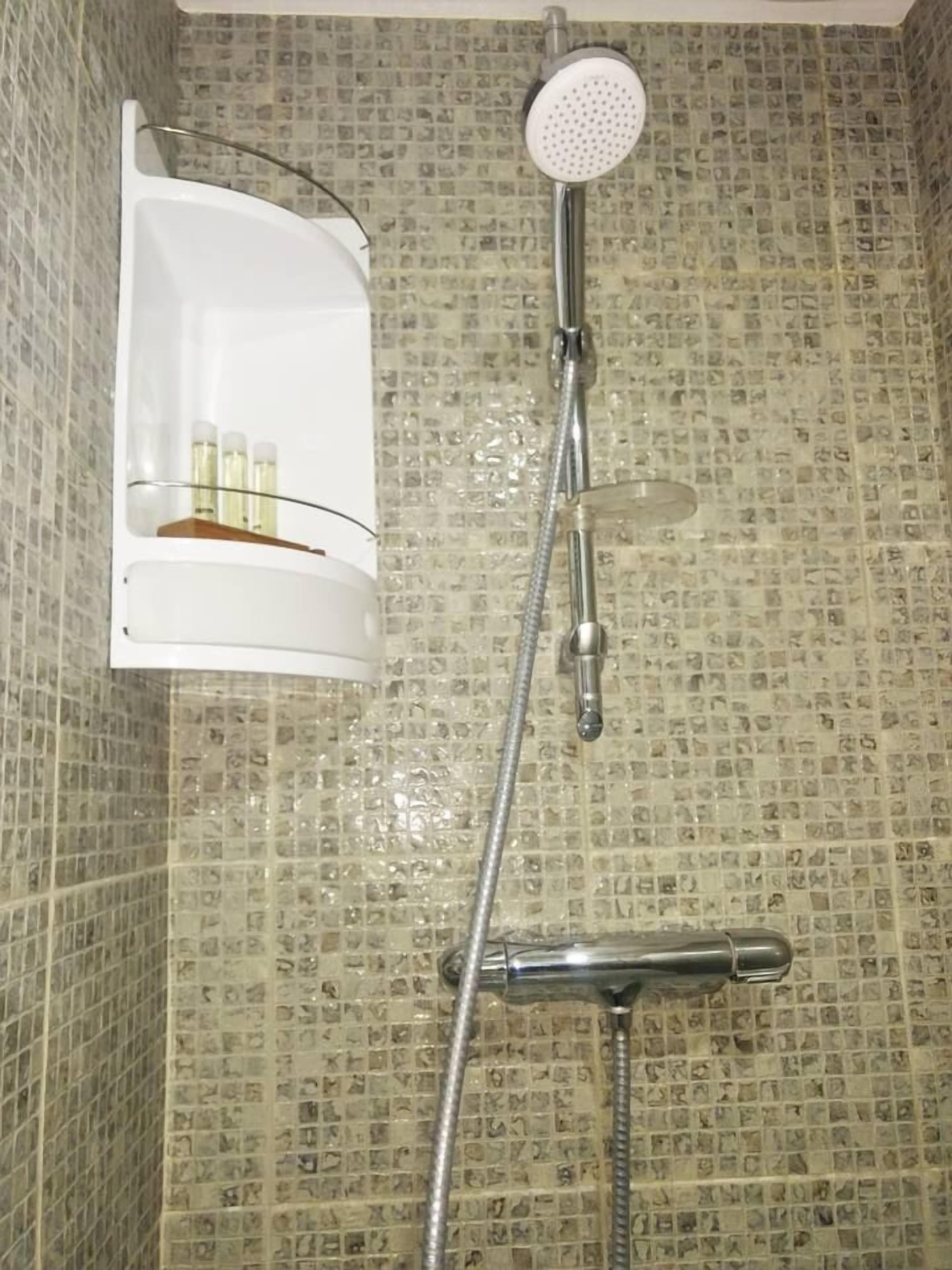 A shower with a handheld showerhead and a wall-mounted faucet.