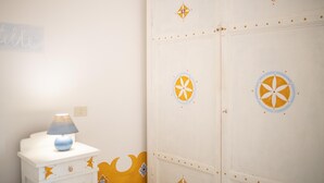 Une pièce avec un meuble blanc orné de motifs décoratifs, une lampe bleue posée sur le dessus, et un mur sur lequel on peut lire une partie d’une inscription : « telle ».