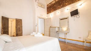 A hotel room with a large bed, a wooden door, a vanity with a mirror, and a television on the wall. - Camera Saggezza - Racale (Racale)