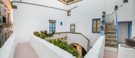 A narrow courtyard with white walls, blue doors, and a small staircase leading to an upper level.