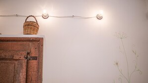 A rustic wooden cabinet with a basket on top, a string of lights, and a wall with a simple floral design. - Camera Fiori Di Pesco - Racale (Racale)