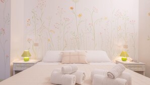 A neatly made bed with white linens and rolled towels, two bedside tables with lamps, and a floral wallpaper design. - Camera Fiori Di Pesco - Racale (Racale)