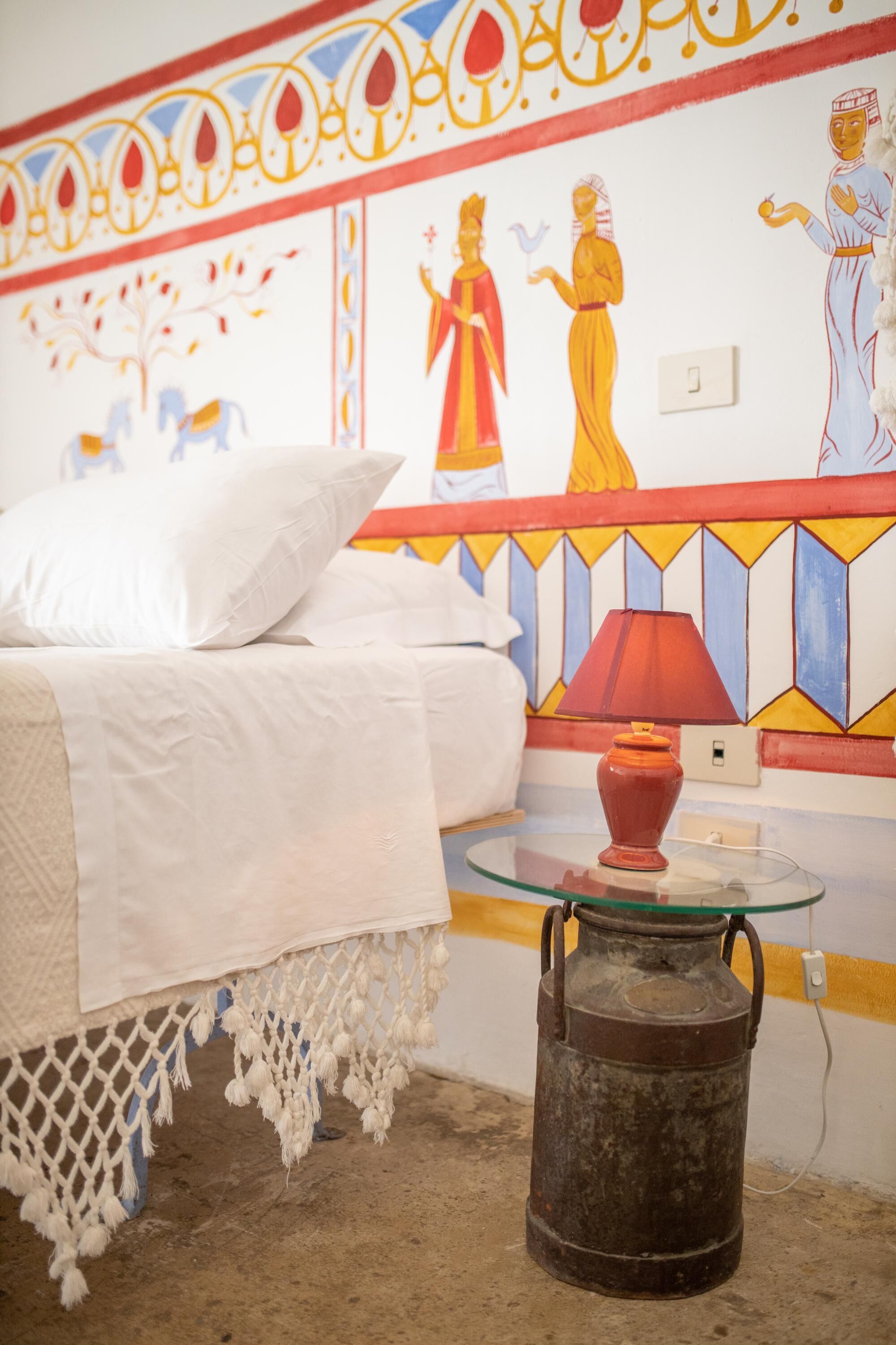A bed with white bedding, a red lamp, and a decorative wall with a geometric pattern.
