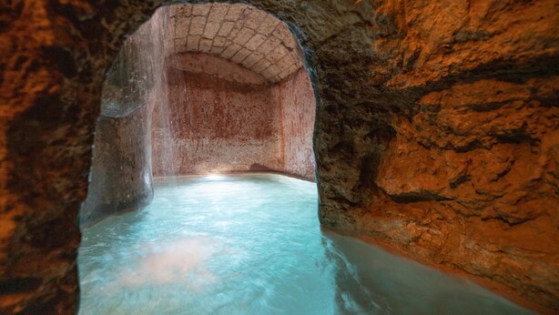 Un tunnel aux parois en pierre, avec une piscine au bout.