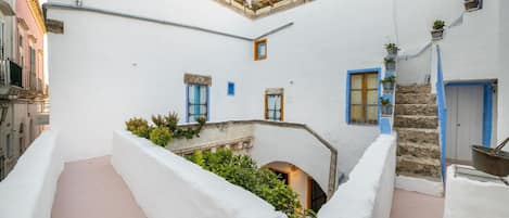 A narrow courtyard with white walls, blue doors, and a small staircase leading to an upper level.