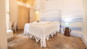 A room with a bed, a chair, a small table with a lamp, and a wall with a painted design. - Camera Onda Dorata - Racale (Racale)