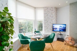 A dining area with a round table, green chairs, and a TV on the wall.