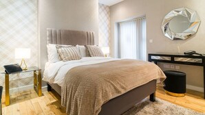 Ein modernes Schlafzimmer mit einem großen Bett, einem Nachttisch mit Lampe, einem Spiegel an der Wand und einem schwarzen Schreibtisch mit Stuhl.