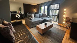 A modern living room with a grey sectional sofa, a wooden coffee table, and a black leather couch. - Spacious 2 Bd Apt w/Fast Wifi+CableTV+Audio System (Cardiff)