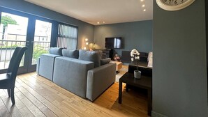 A modern living room with a grey sofa, a TV, and a clock on the wall. - Spacious 2 Bd Apt w/Fast Wifi+CableTV+Audio System (Cardiff)