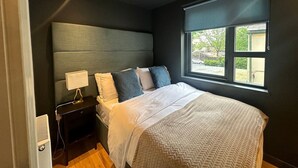 A bedroom with a bed, bedside table, lamp, and a window with a view of greenery. - Spacious 2 Bd Apt w/Fast Wifi+CableTV+Audio System (Cardiff)