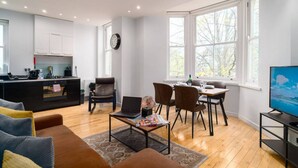 A modern living room with a dining area, a kitchen, and a TV. - Superb Modern 1 Bedroom Apt | Cocoon Dbl Sofa Bed (Cardiff)