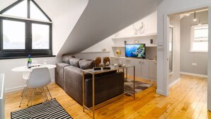 Een modern loft appartement met een hoogslaper, een woonruimte met een bank en televisie, een eethoek met een tafel en stoelen, en een keuken met een raam.