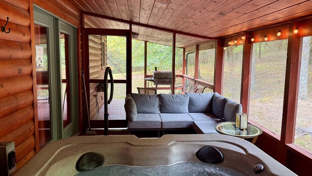 A log cabin with a hot tub, a sofa, and a table with a lamp.