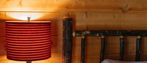 Una cama de madera con ropa blanca de cama, una lámpara rayada de rojo sobre una mesita de noche de madera, y dos cuadros con motivos florales en la pared.