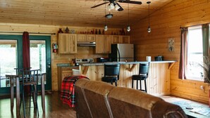 A cozy cabin-style kitchen with wooden walls, a bar area, and a dining space with a plaid tablecloth.