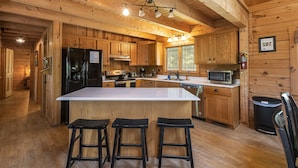 A wooden cabin kitchen with a large island, bar stools, and modern appliances.