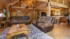 A spacious living area with a high ceiling, wooden beams, and a cozy fireplace. There are two leather sofas and a coffee table.