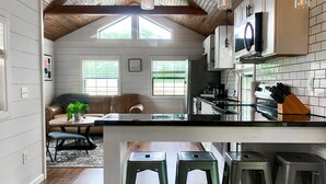 A kitchen with a wooden ceiling, white cabinets, a black countertop, and a TV mounted above the stove. - Upscale Cabin w/ Beach Near Lake of Egypt (Marion)