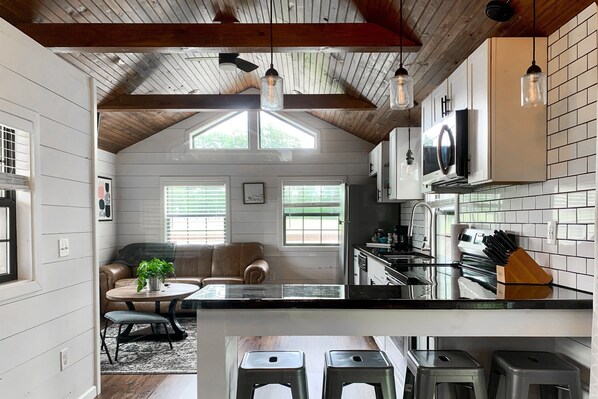 A modern kitchen with a black countertop, stainless steel appliances, and hanging pendant lights.