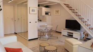 A modern living room with a white sofa, a glass coffee table, and a TV on a white stand. - kaDevi Holiday home -full center, private garage and bikes (Sanremo)