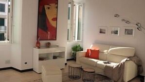 A modern living room with a white sofa, a glass coffee table, and a red accent pillow. There is a large poster on the wall and a floor lamp. - kaDevi Holiday home -full center, private garage and bikes (Sanremo)