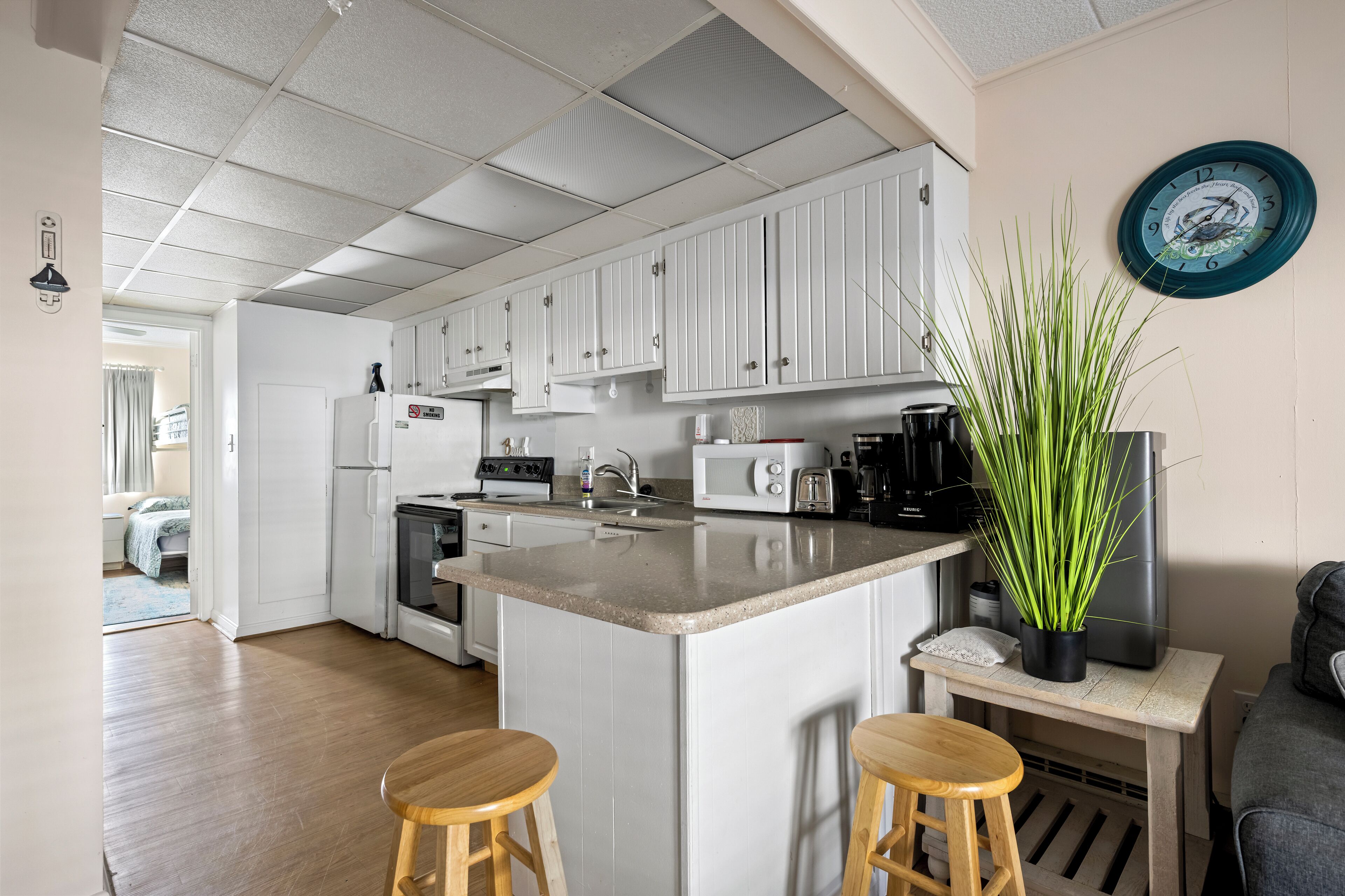 A modern kitchen with white cabinets, a central island with stools, a microwave, and a coffee maker.