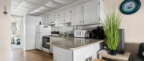 A modern kitchen with white cabinets, a central island with stools, a microwave, and a coffee maker.