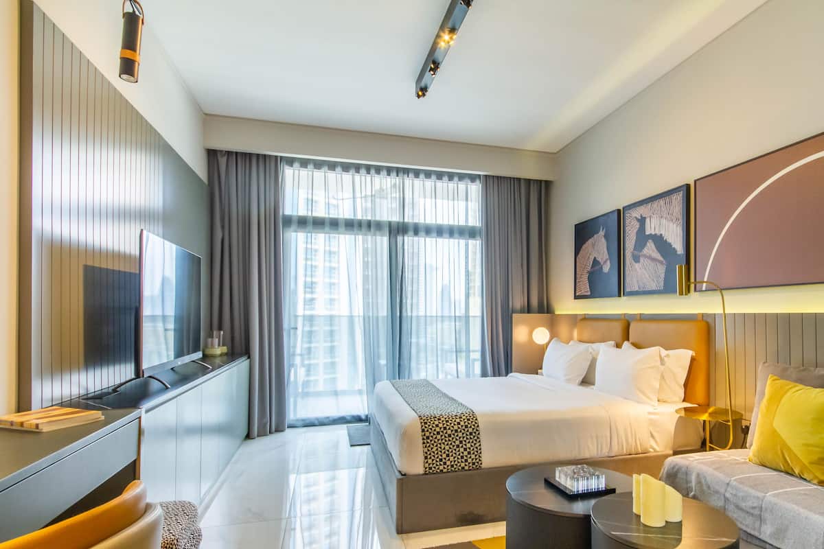 A modern hotel room with a large bed, a sofa, a TV, and a desk.