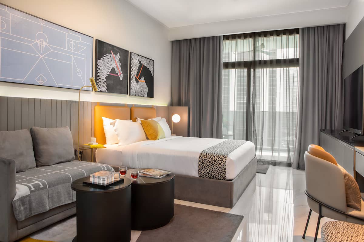 A modern hotel room with a large bed, a sofa, a desk, and a TV.