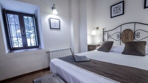 A bedroom with a bed, a laptop, a window, a radiator, and wall-mounted lights. - Posada Peña Pintada by Vivere Stays (Cercedilla)