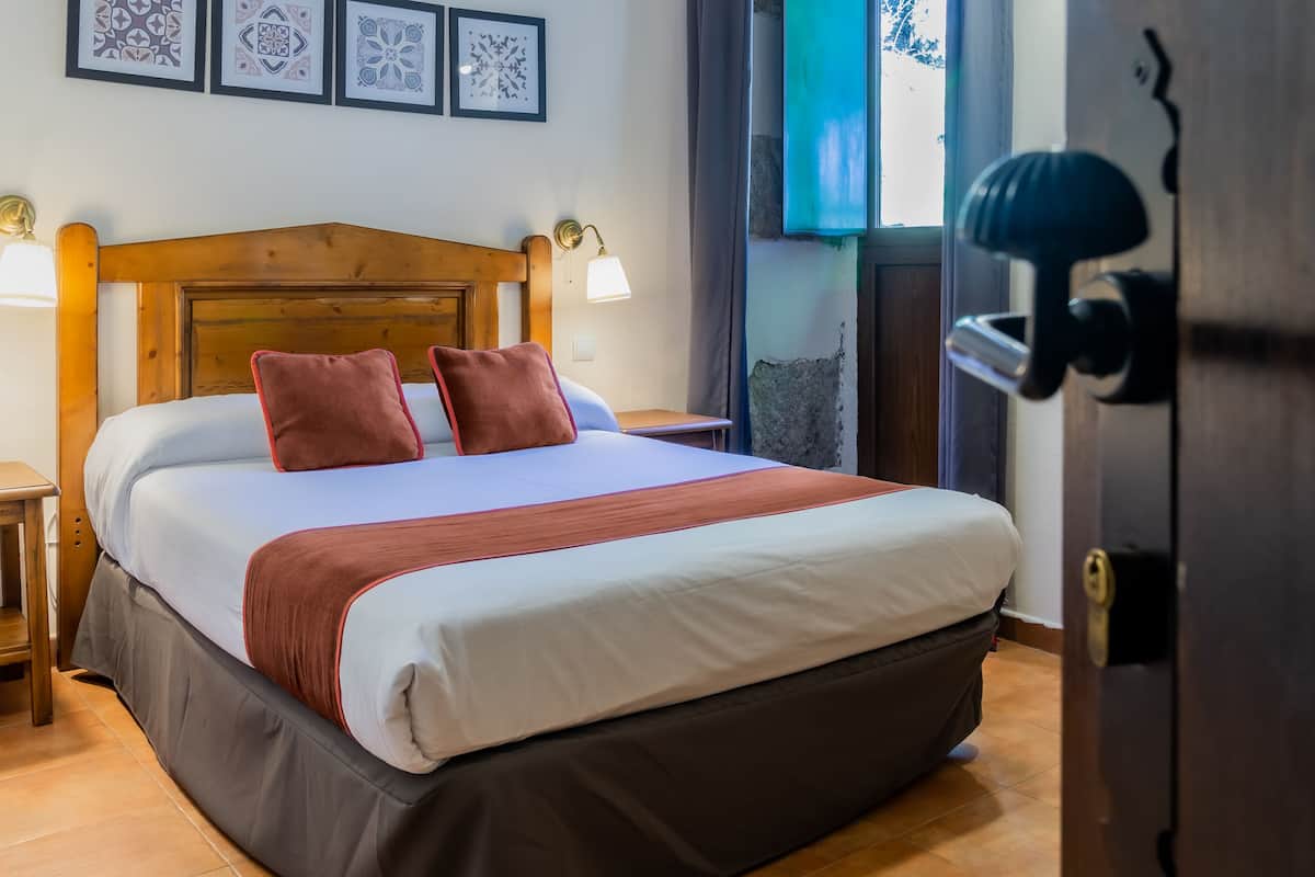 Un lit bien fait, avec une tête de lit en bois, une table de chevet et une petite table à poser près du lit.