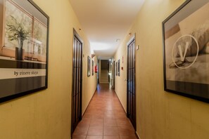 A hallway with framed artwork on the walls, doors, and a potted plant on the left. - Posada Peña Pintada by Vivere Stays (Cercedilla)