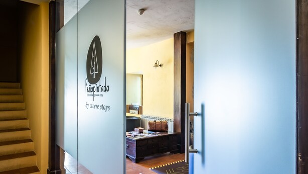 A hotel entrance with a glass door, a staircase, and a reception area with a counter and a sofa. - Posada Peña Pintada by Vivere Stays (Cercedilla)