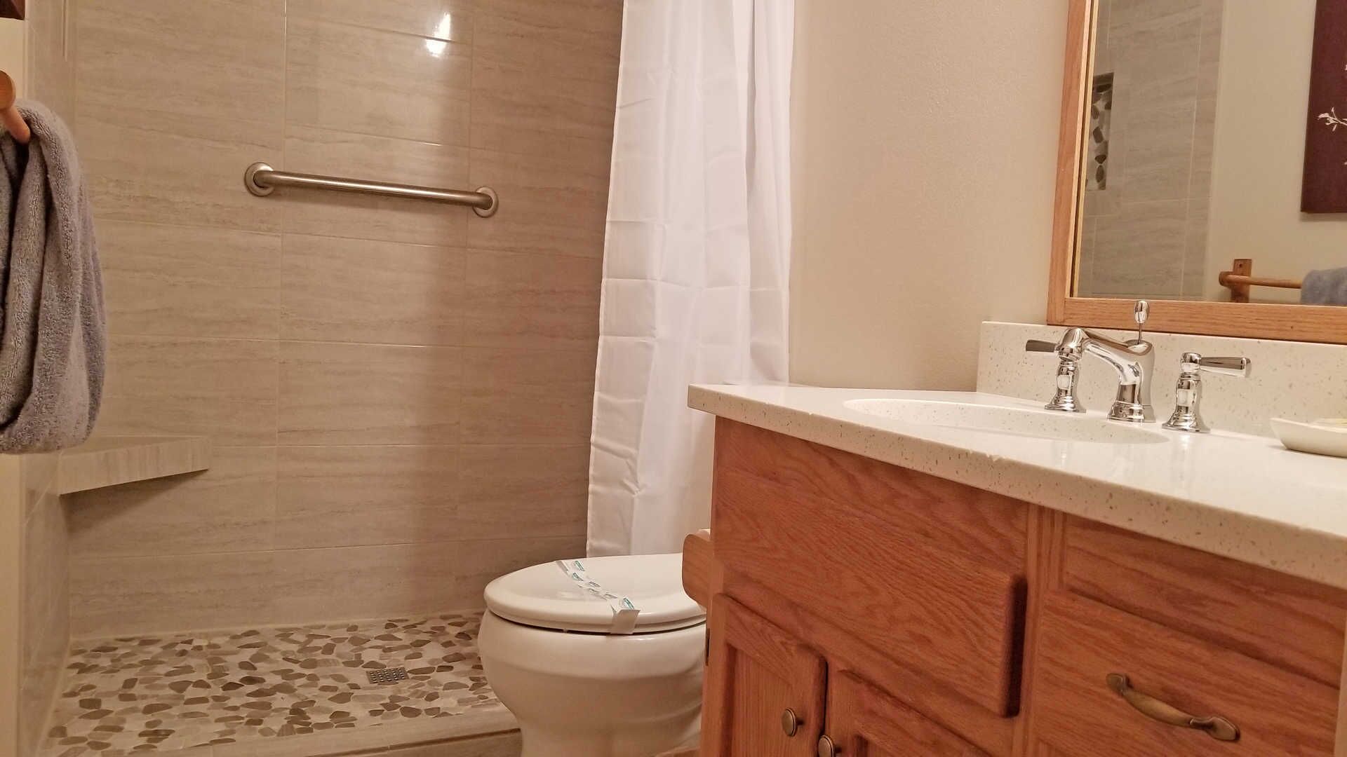 A bathroom with a shower, toilet, and vanity with a mirror.