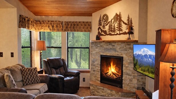 Una sala de estar acogedora con chimenea, un sillón de cuero, un sofá y un televisor colocado sobre la chimenea.