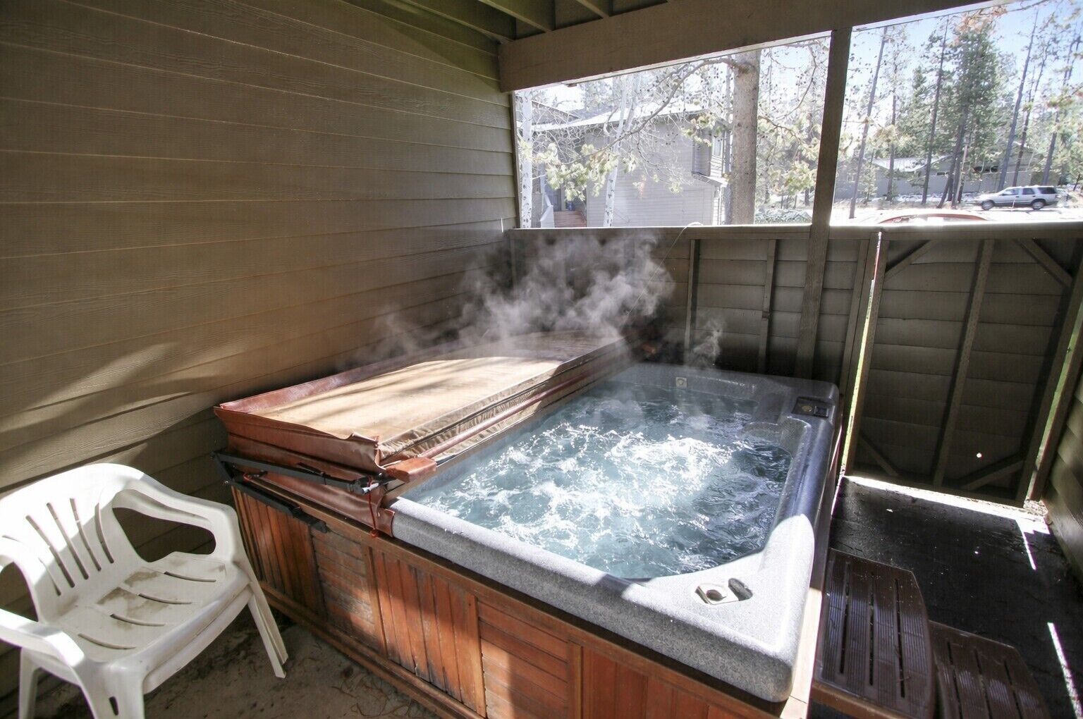 A hot tub with steam, a white plastic chair, and a wooden deck.